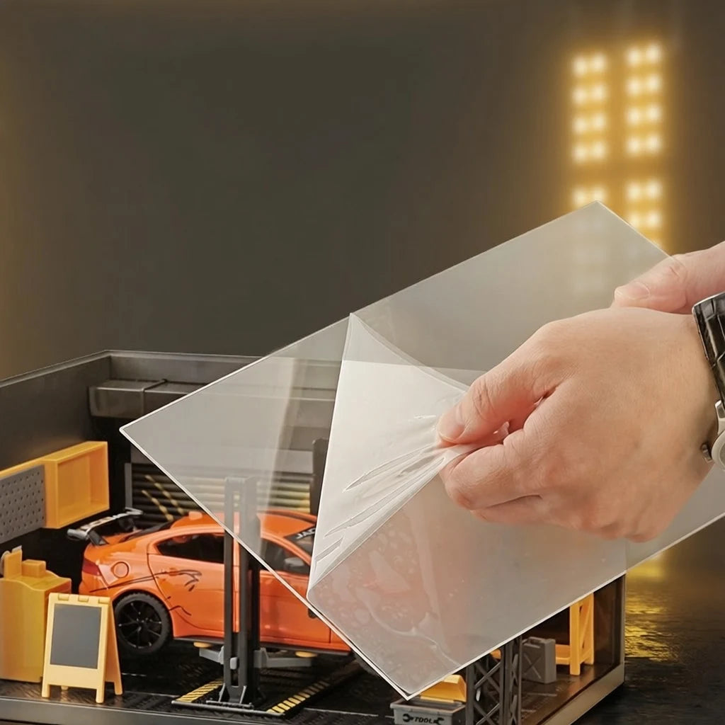 A hand peeling the protective film off the clear acrylic cover of the 1:24 garage display case