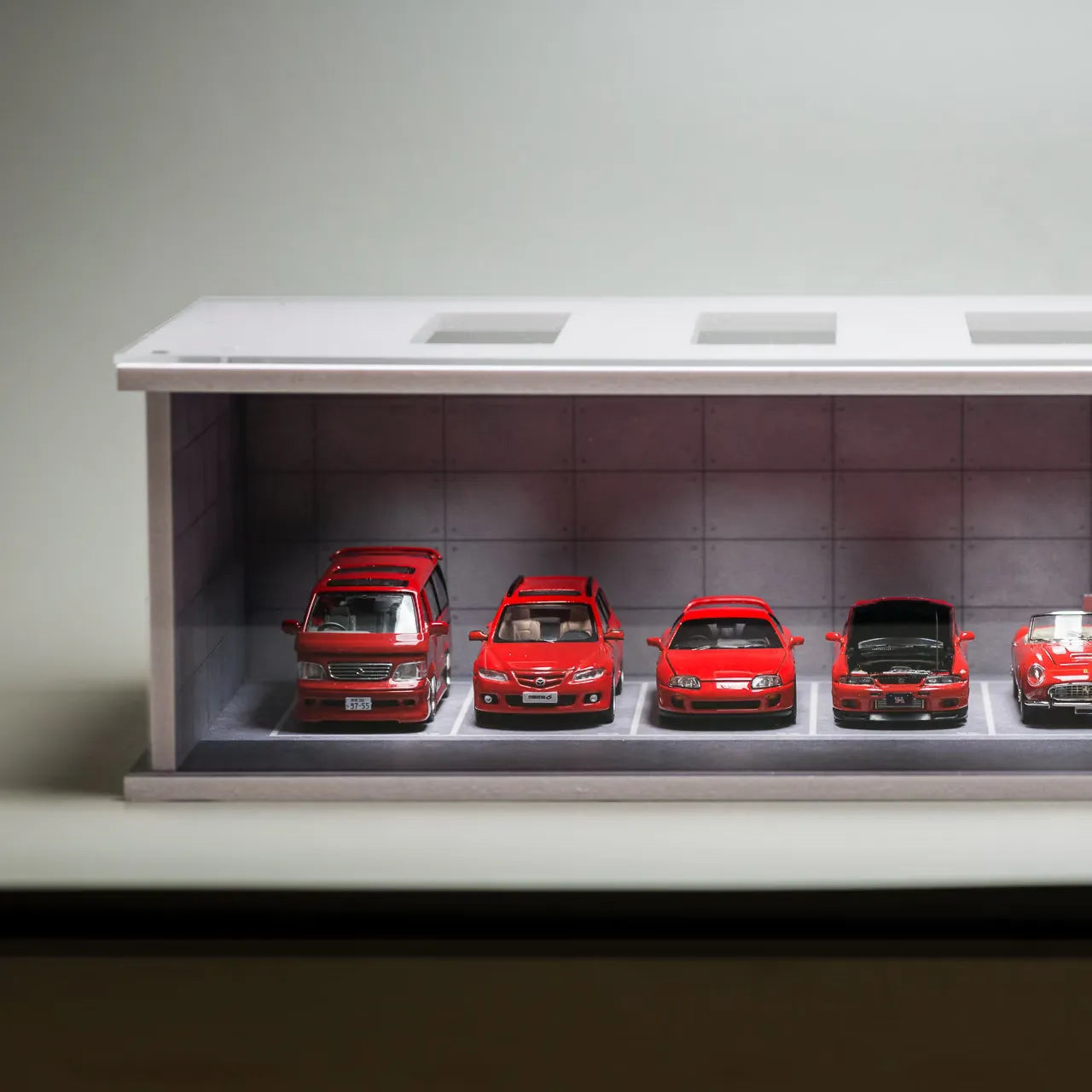 Collection of red model cars displayed in a case with a neutral background